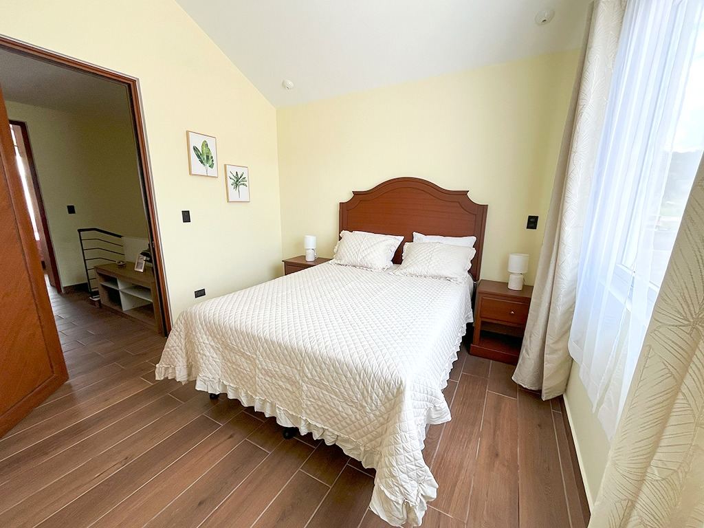 Dormitorio principal con cama matrimonial, mesas de noche y ventanal con cortinas