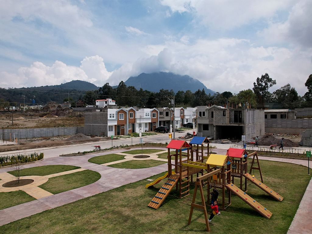 Parque infantil y jardines con casas al fondo y volcán entre nubes